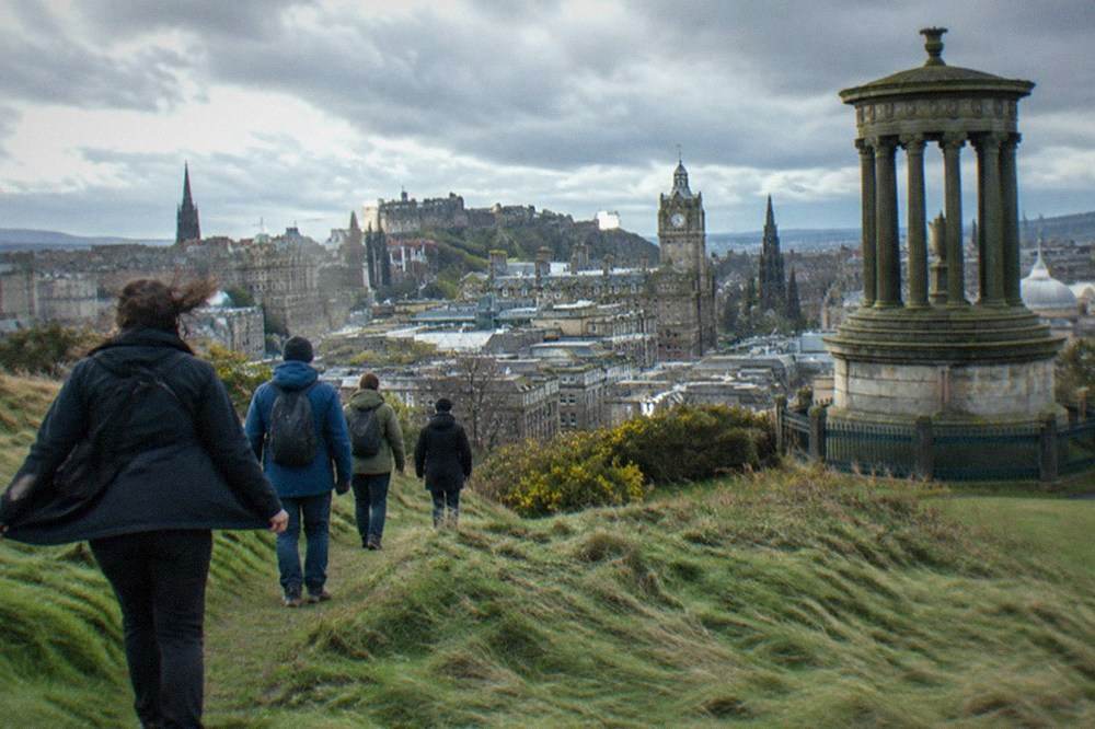 Grass slope and rocky path on a hill above city rooftops under a cloudy sky