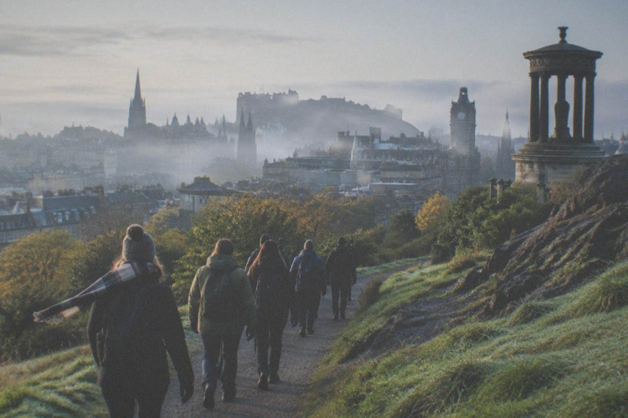 Edinburgh Old Town rooftops and a church spire seen from a green hillside
