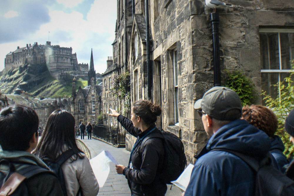 A guide holding up a printed map while visitors gather on the Royal Mile in Edinburgh