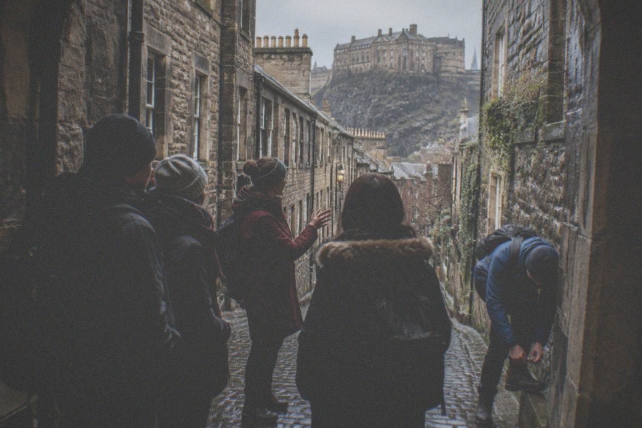 A guide speaking to a small group gathered on a cobbled Edinburgh close beneath old stone buildings