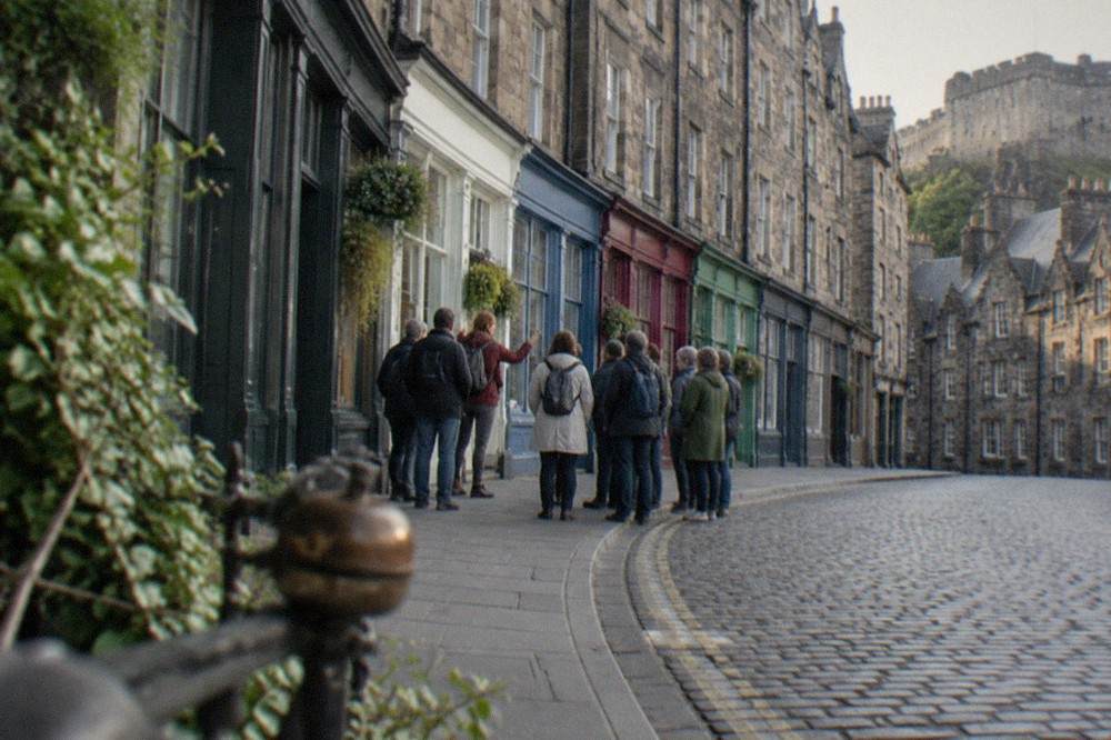 A curved Edinburgh street of colourful shopfronts descending toward a market square