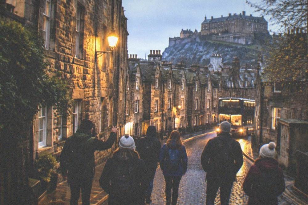 A lit bus moving along a wet Edinburgh street in the evening
