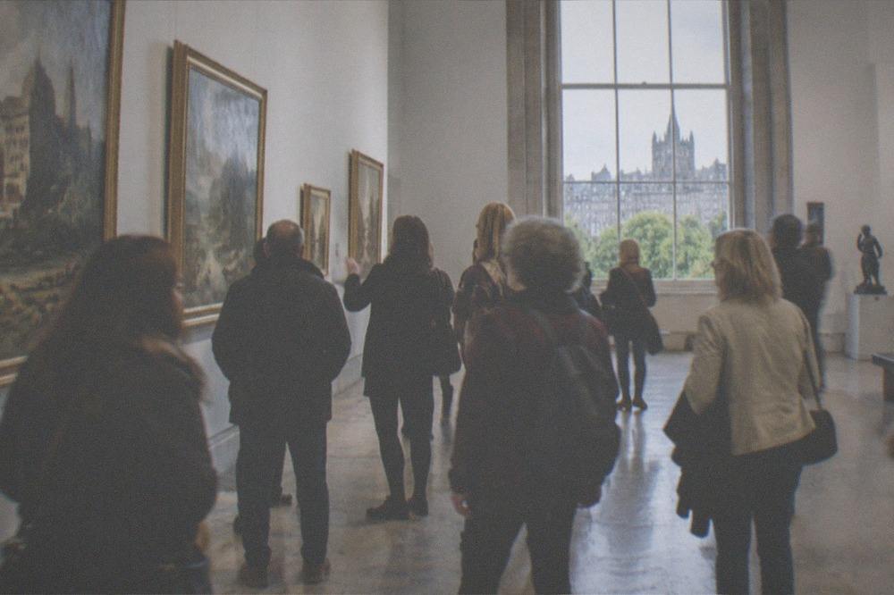 A bright gallery hall with paintings hung on the walls and visitors walking through