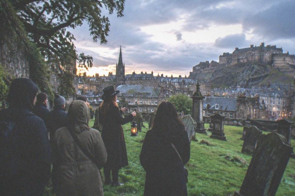 Old graveyard at dusk with weathered headstones, wet grass and dark rain clouds above the city rooftops