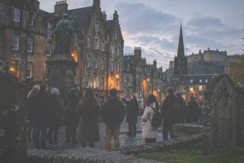 Greyfriars Kirkyard at dusk with weathered gravestones and the city skyline behind