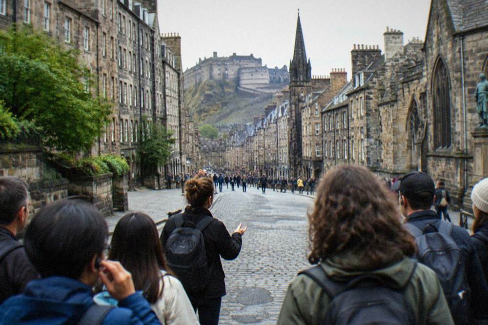 A guided walking group gathered on a cobbled Royal Mile street beside tall stone buildings